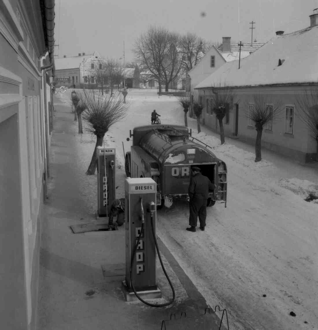 Herrengasse und der Hauptplatz  im Winter mit den Zapfsäulen der Tankstelle vor der Sparkasse, dem Kaufhaus und der Tabak Trafik Radnetter und dem Gasthof Bauer