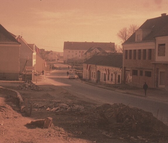 Platz vor dem Kastell und der Hauptschule mit den beflaggten Häusern der Familien Csar, Radanovits, Sabara, Konskr, Senninger, Bauer und Pieber